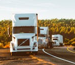 Three semi trucks driving on a highway through a forested landscape in Arizona.