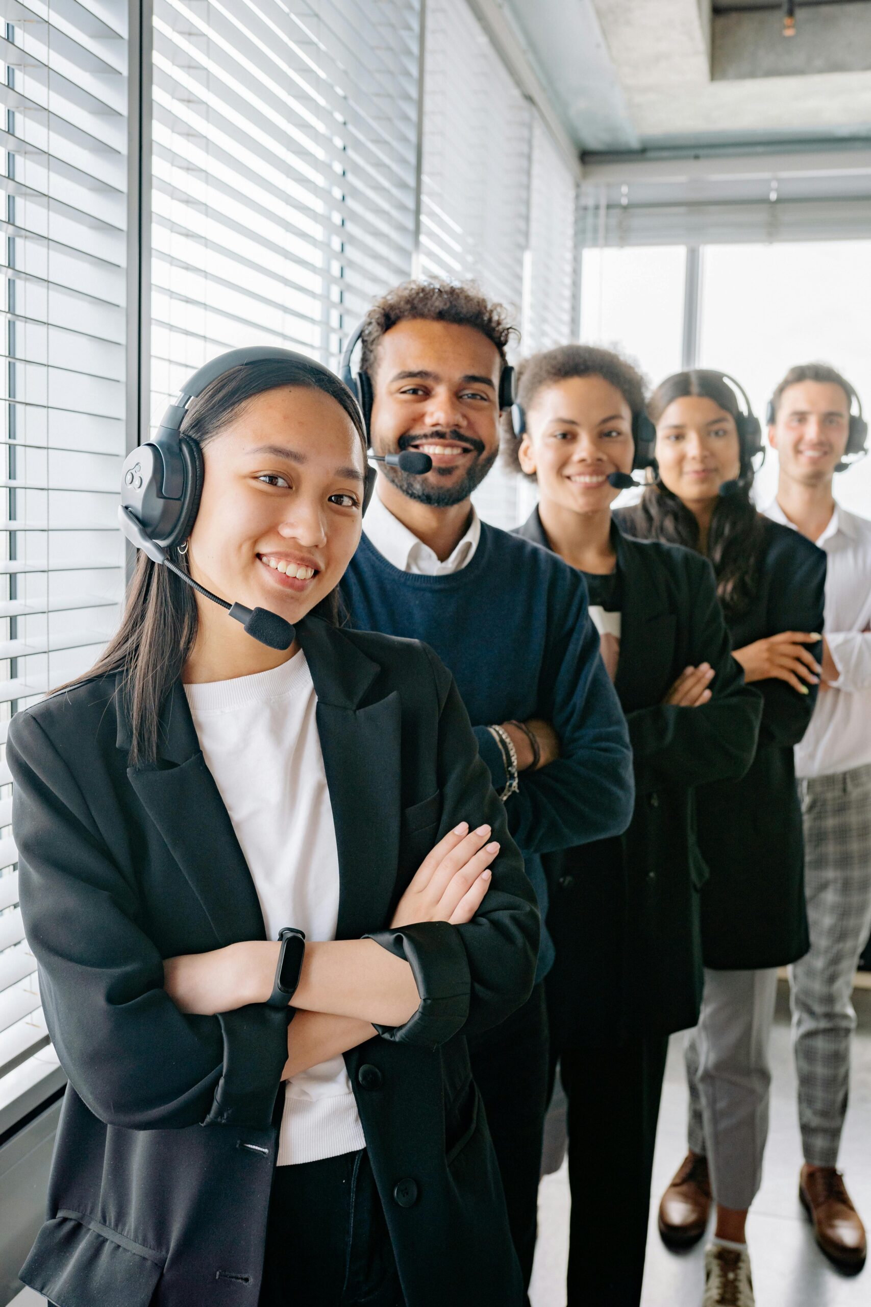 A diverse group of call center agents smiling and standing in line with headsets in an office.